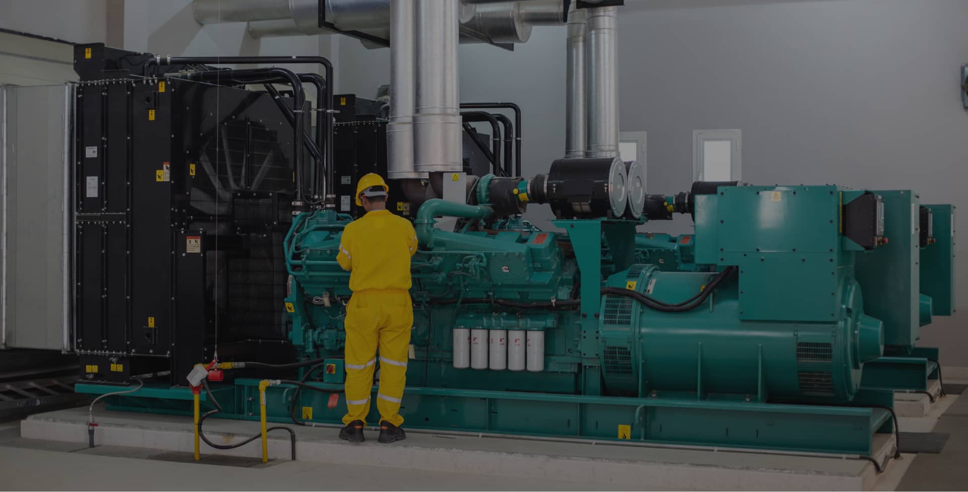 Technician in yellow uniform working on a large green industrial generator inside a facility.