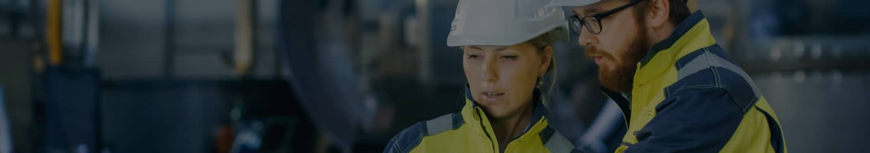 Two engineers in safety gear discussing a project in an industrial setting.